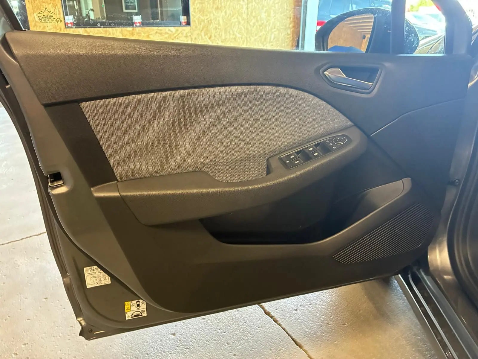 Vue intérieure côté gauche de la porte avant d'une Renault Clio gris schiste avec commandes des vitres et tissu gris.