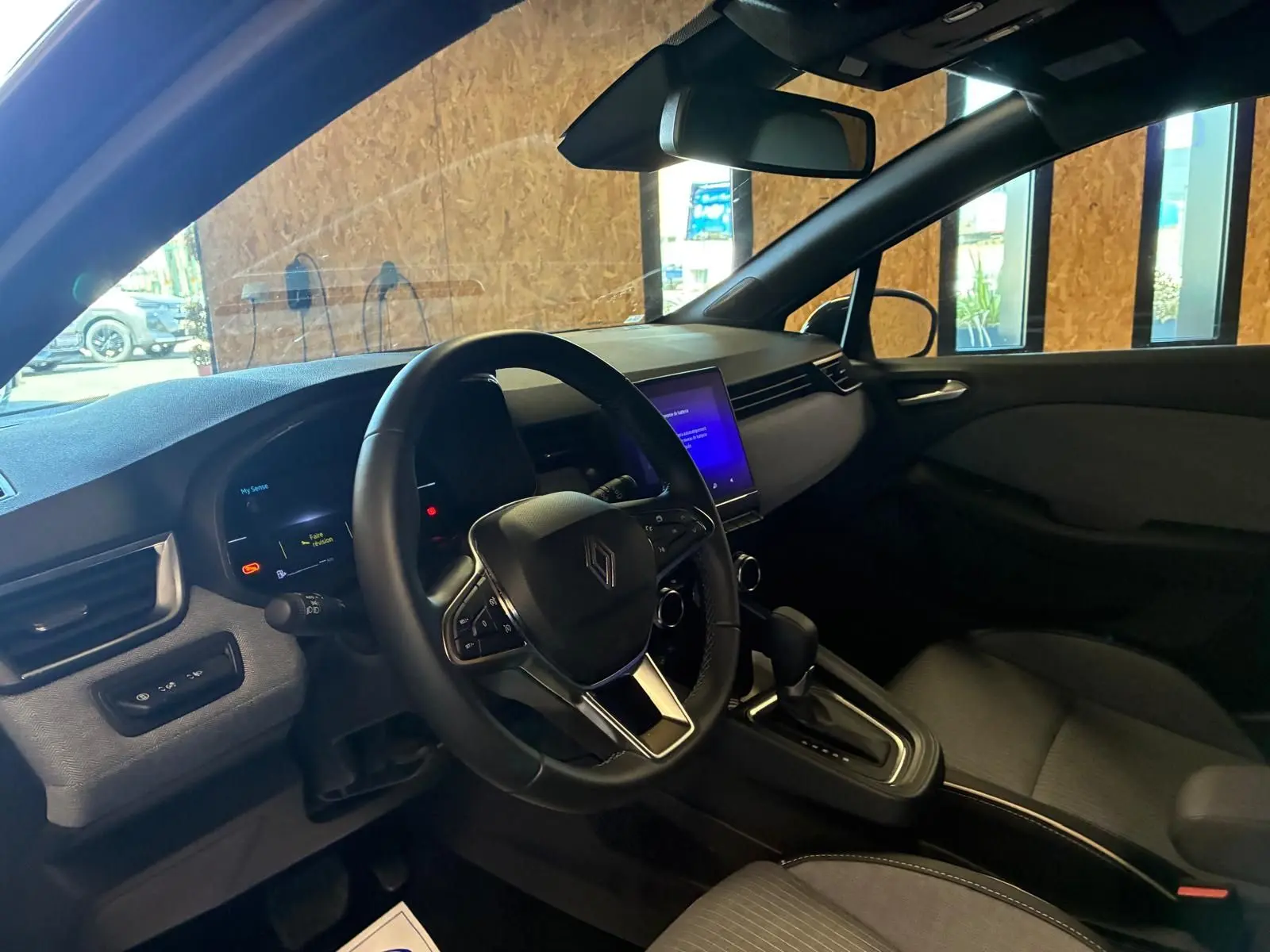 Vue intérieure côté conducteur de la Renault Clio 2025 gris schiste, avec volant multifonction et écran tactile central allumé.