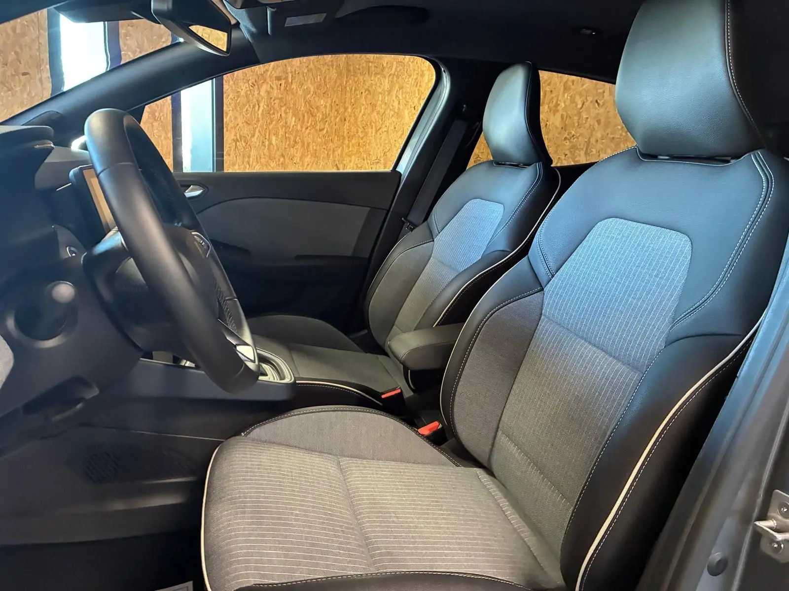 Vue intérieure côté conducteur de la Renault Clio 2025, sièges tissu gris clair avec contours en cuir noir.
