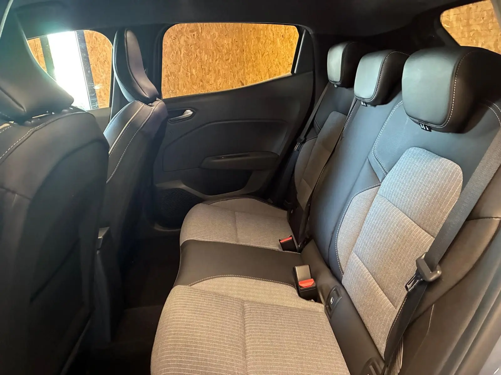 Vue intérieure arrière de la Renault Clio 2025, sièges tissu gris clair avec surpiqûres et garnitures noires.
