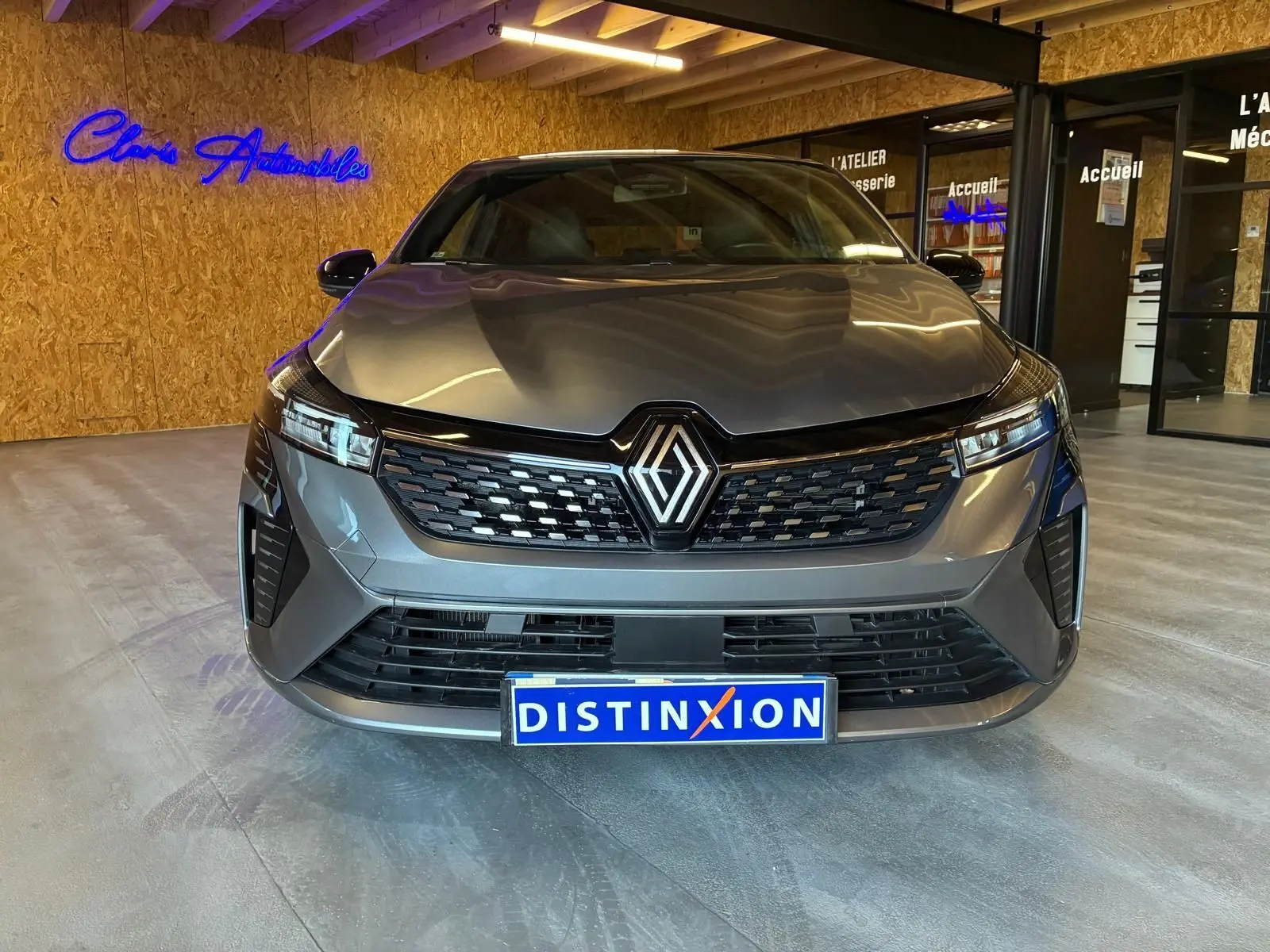 Vue frontale d'une Renault Clio 2025 gris schiste, avec calandre noire et logo Renault lumineux, en intérieur showroom.