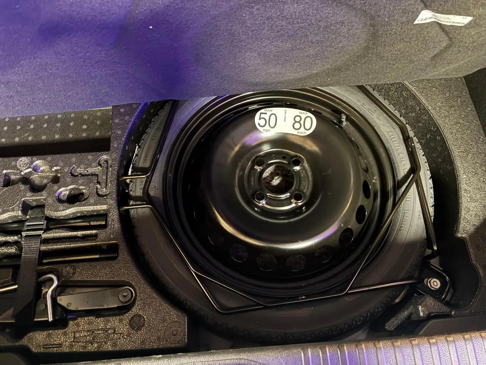 Vue rapprochée de la roue de secours noire et des outils de bord dans le coffre d'une Renault Clio gris schiste 2025.