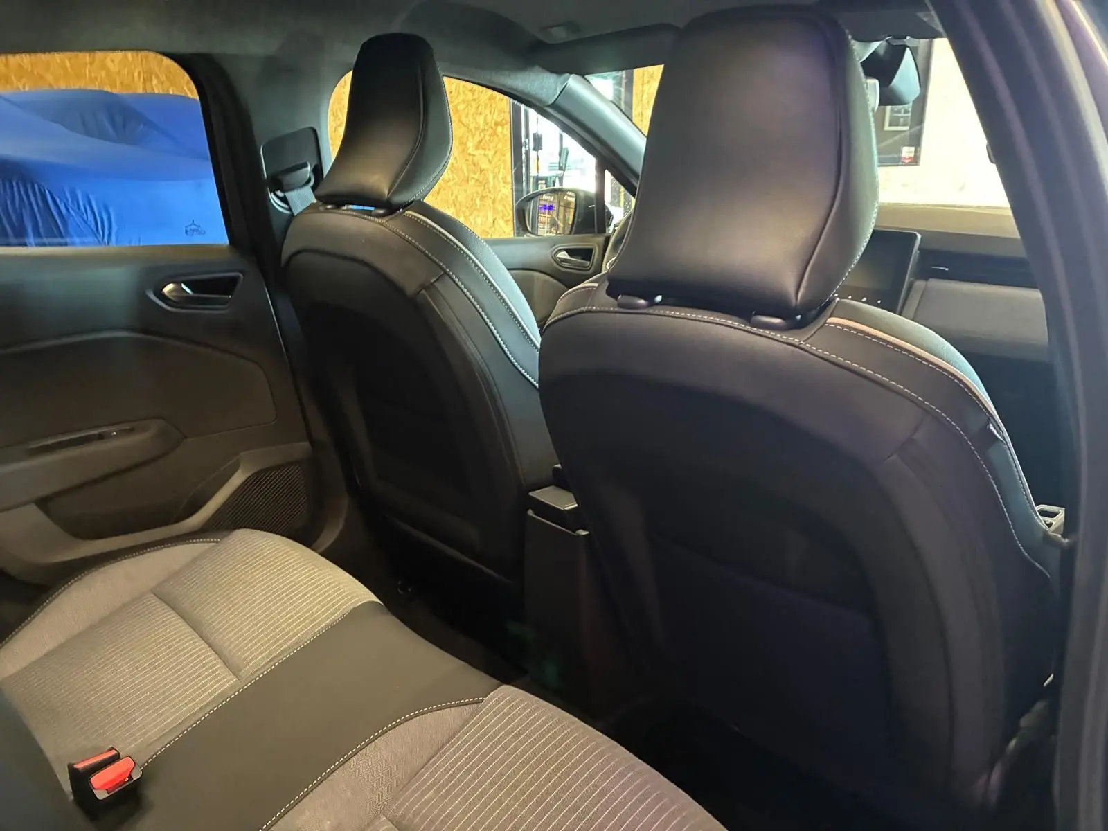 Vue intérieure arrière de la Renault Clio 2025, sièges tissu gris noir avec surpiqûres blanches, ambiance sobre et moderne.
