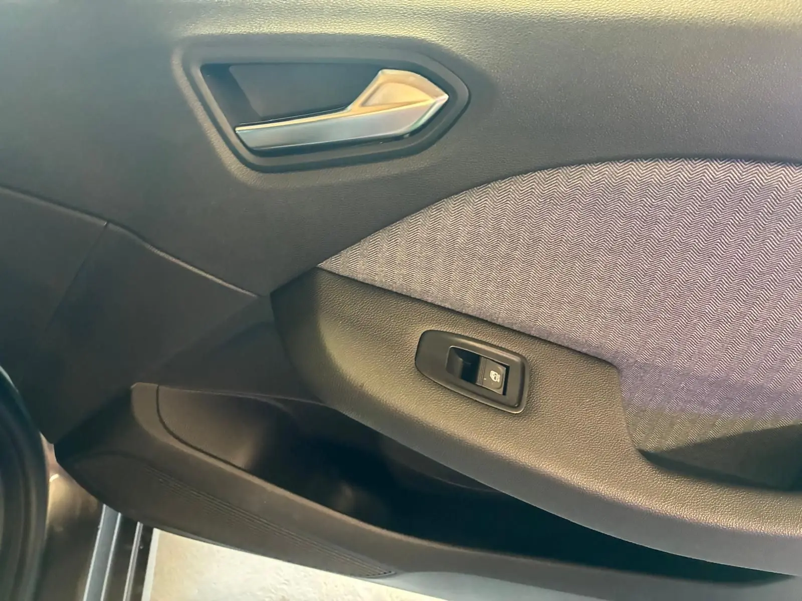 Détail de la porte côté gauche de la Renault Clio 2025 gris schiste, avec poignée argentée et bouton de commande de vitre.