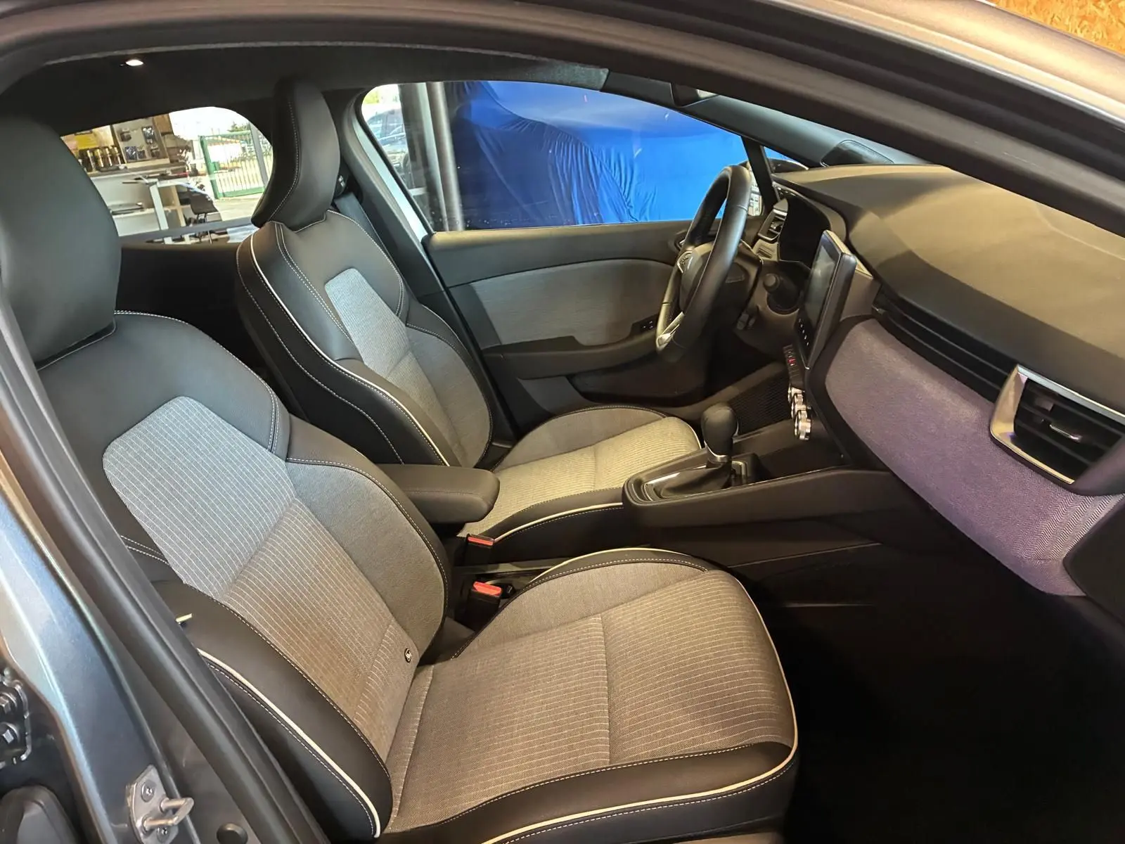 Intérieur de la Renault Clio 2025 en gris schiste, vue côté gauche sur les sièges tissu gris clair avec surpiqûres blanches.