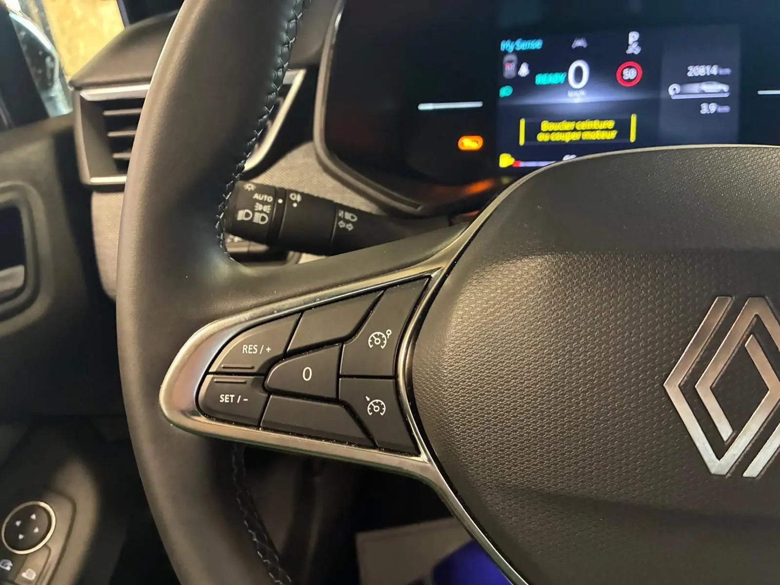 Gros plan sur le volant côté gauche de la Renault Clio gris schiste, avec commandes de régulateur de vitesse et tableau de bord numérique.