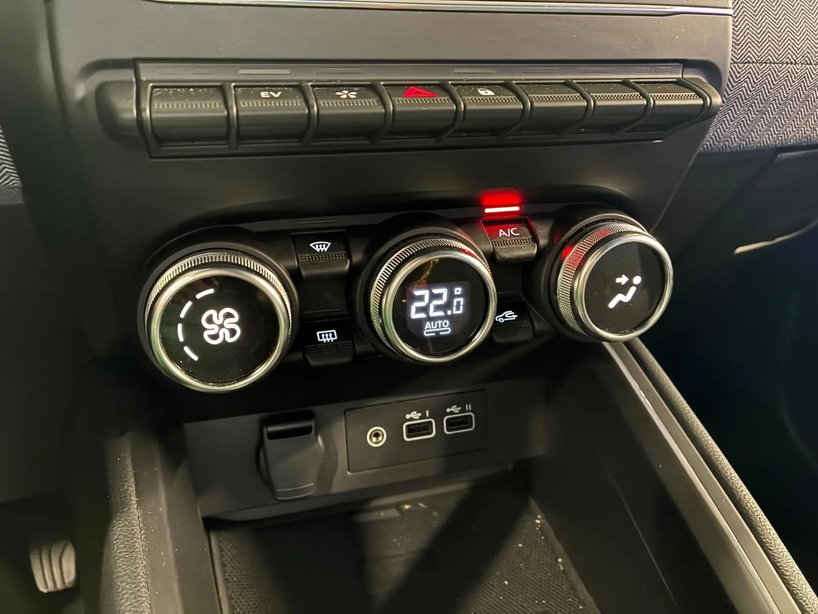 Gros plan sur la console centrale de la Renault Clio 2025, boutons de climatisation numériques et connectiques USB visibles.