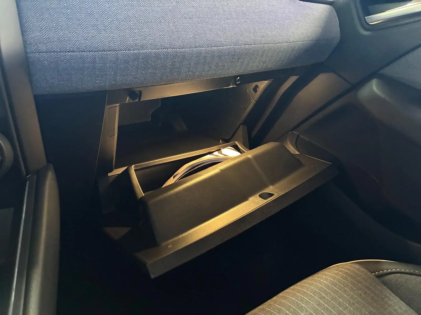 Gros plan sur la boîte à gants ouverte côté passager de la Renault Clio 2025, intérieur tissu gris noir.