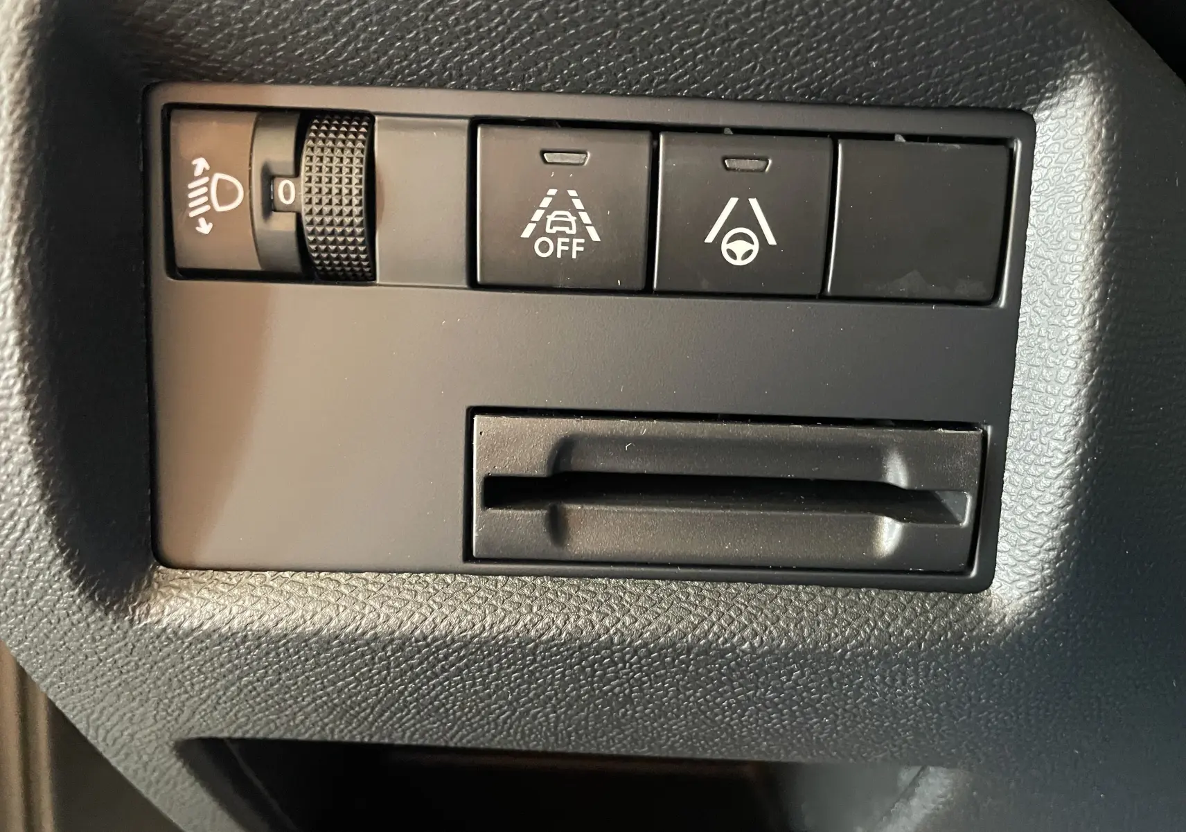 Gros plan sur les commandes noires du tableau de bord du Citroën C5 Aircross hybride 2025, avec réglage des phares et aides à la conduite.
