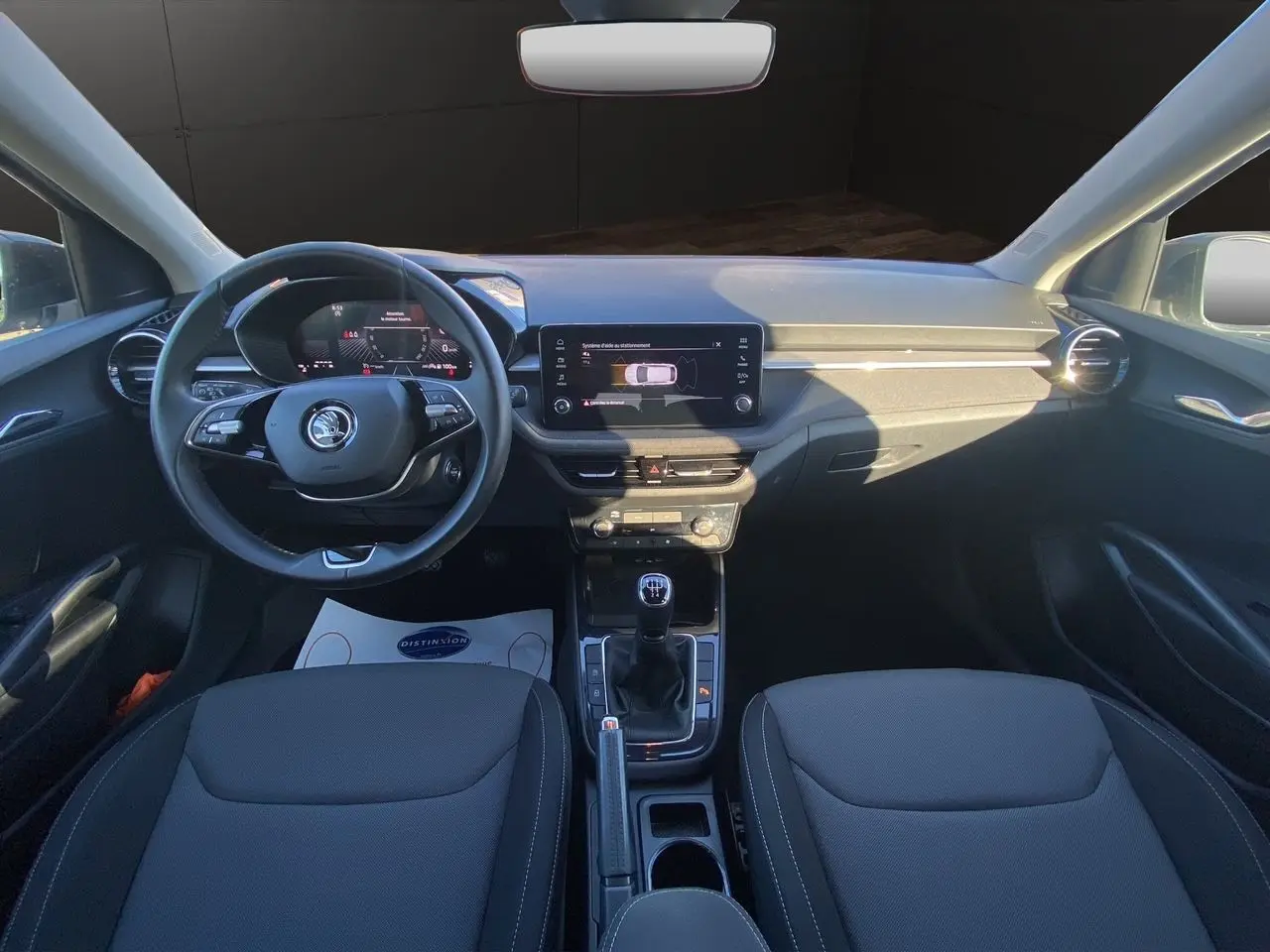 Intérieur avant de la Skoda Fabia 2024 gris/noir, vue frontale sur tableau de bord, volant cuir et écran tactile central.