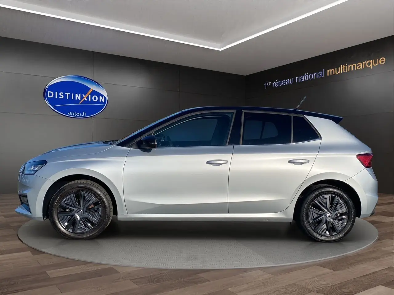 Profil droit d'une Skoda Fabia 2024 gris clair avec toit noir et jantes modernes en concession.