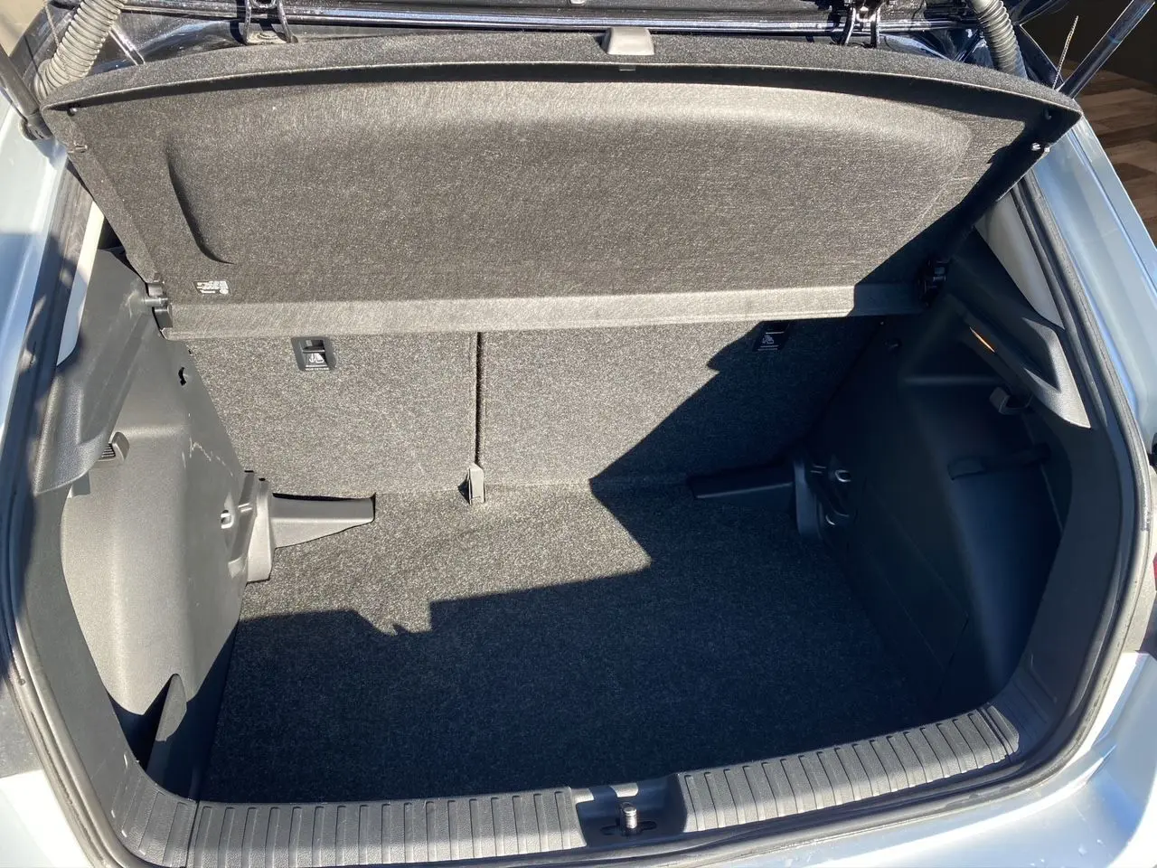 Coffre ouvert vu de dessus d'une Skoda Fabia 2024 gris/noir, montrant l'espace de rangement et la moquette intérieure.