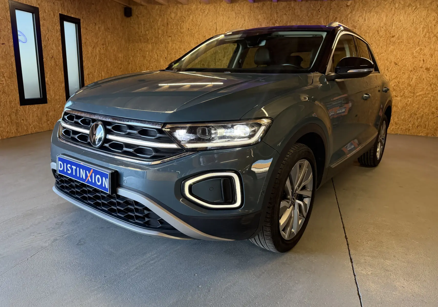 Vue frontale d'un Volkswagen T-Roc bleu 2022 avec calandre chromée et phares allumés en intérieur showroom.