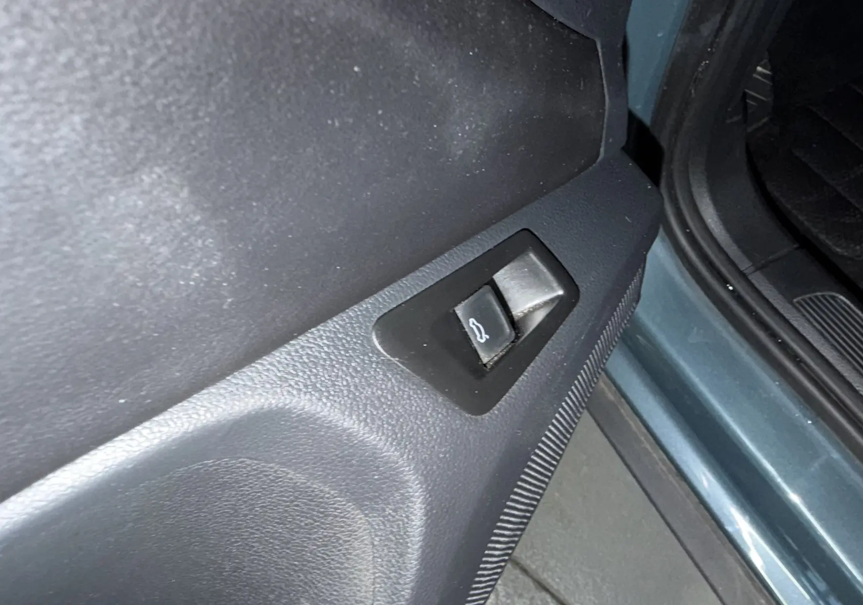 Détail du bouton d'ouverture du coffre sur la portière côté gauche d'un Volkswagen T-Roc bleu 2022.