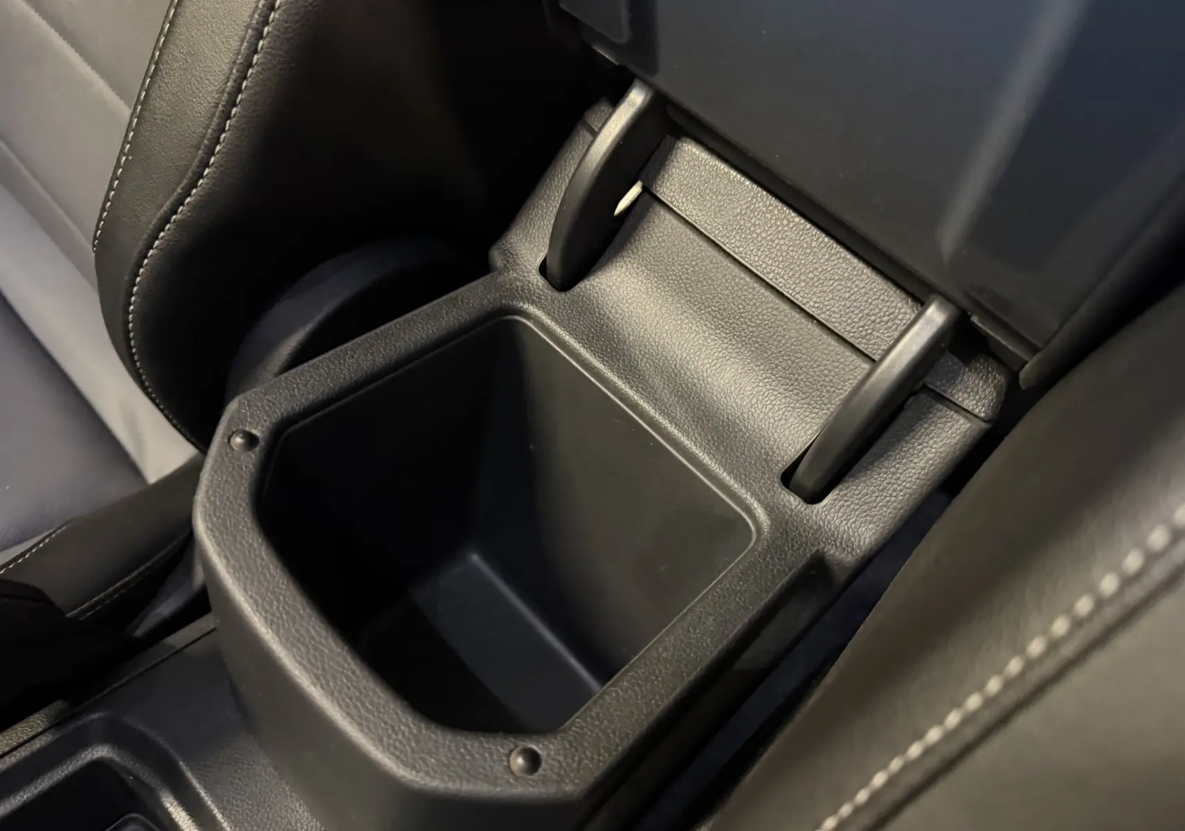 Gros plan sur le rangement central ouvert en plastique noir, entouré de sièges en cuir noir dans un Volkswagen T-Roc 2022.