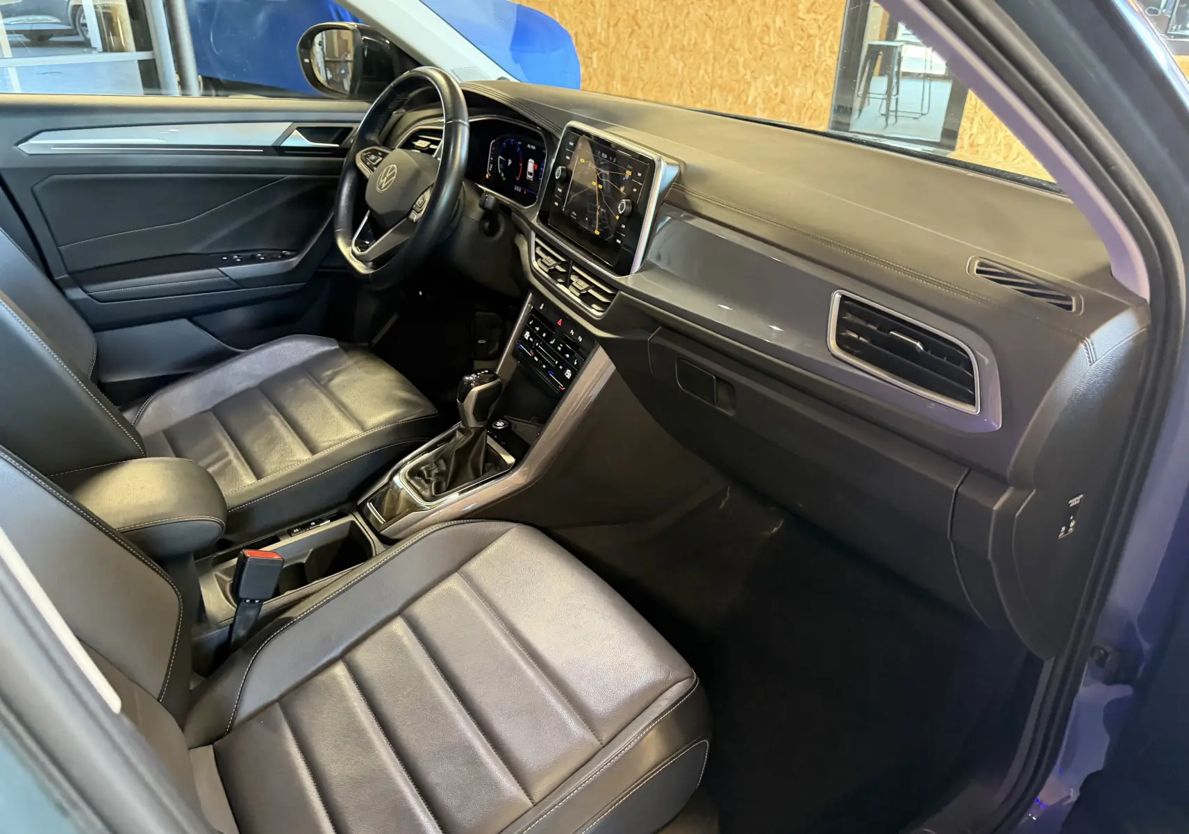 Vue intérieure côté conducteur du Volkswagen T-Roc bleu 2022, avec tableau de bord numérique et sellerie cuir noire.