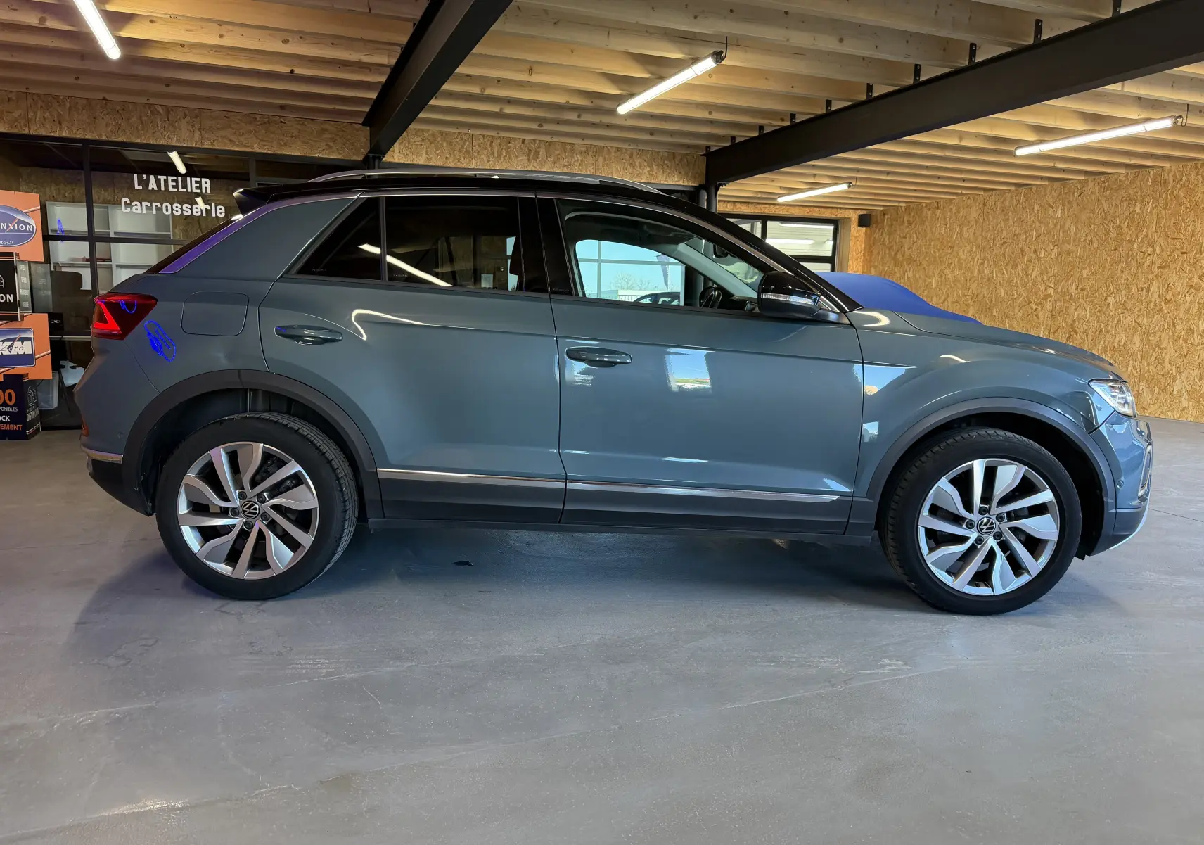 Vue de profil côté gauche d’un Volkswagen T-Roc bleu 2022 dans un garage avec jantes alliage et toit noir.