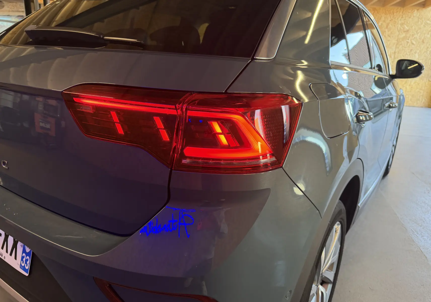 Vue arrière côté droit d’un Volkswagen T-Roc bleu avec feux arrière allumés dans un garage.