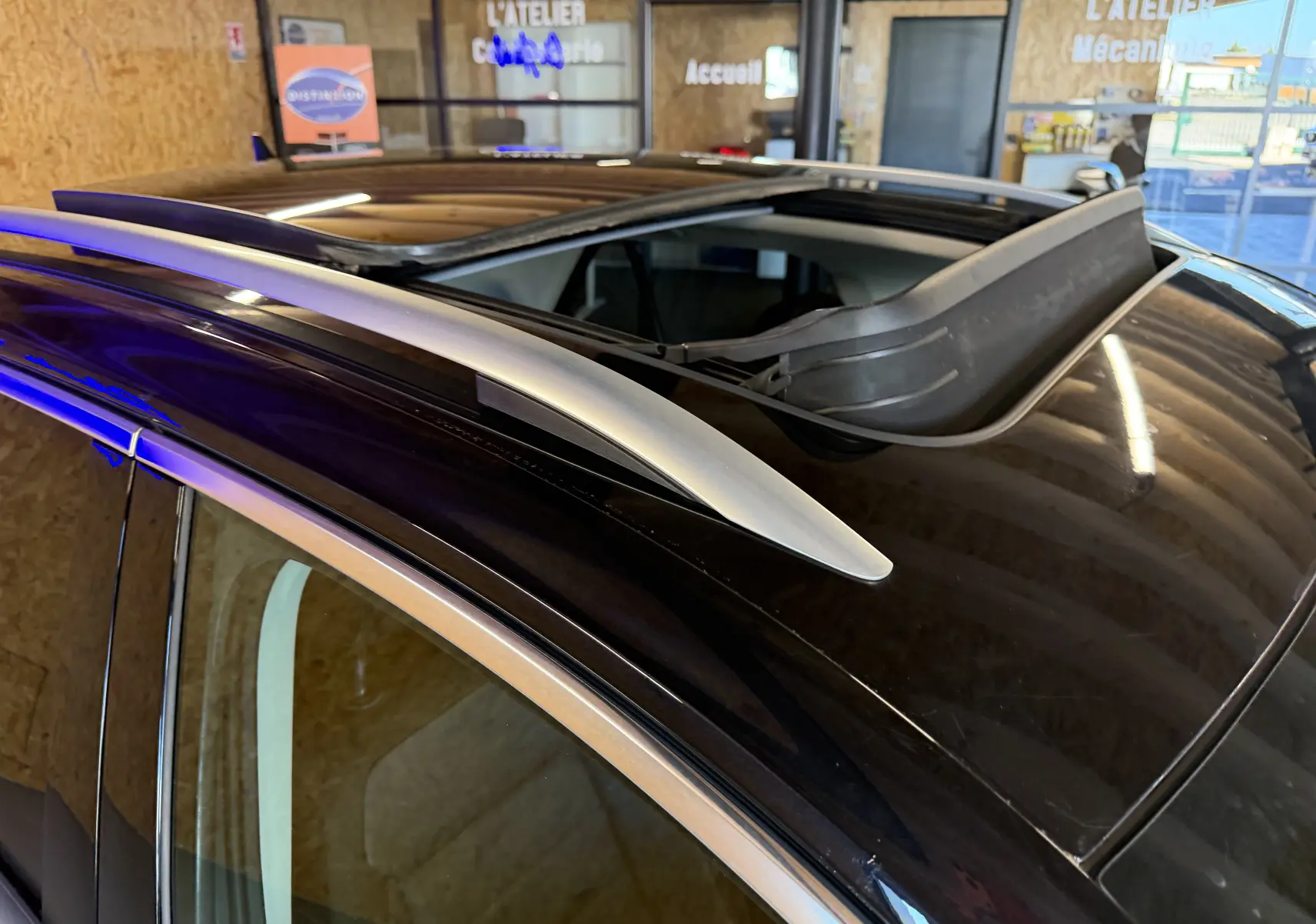 Détail du toit ouvrant panoramique et barres de toit argentées sur Volkswagen T-Roc bleu, vue en plongée intérieure.