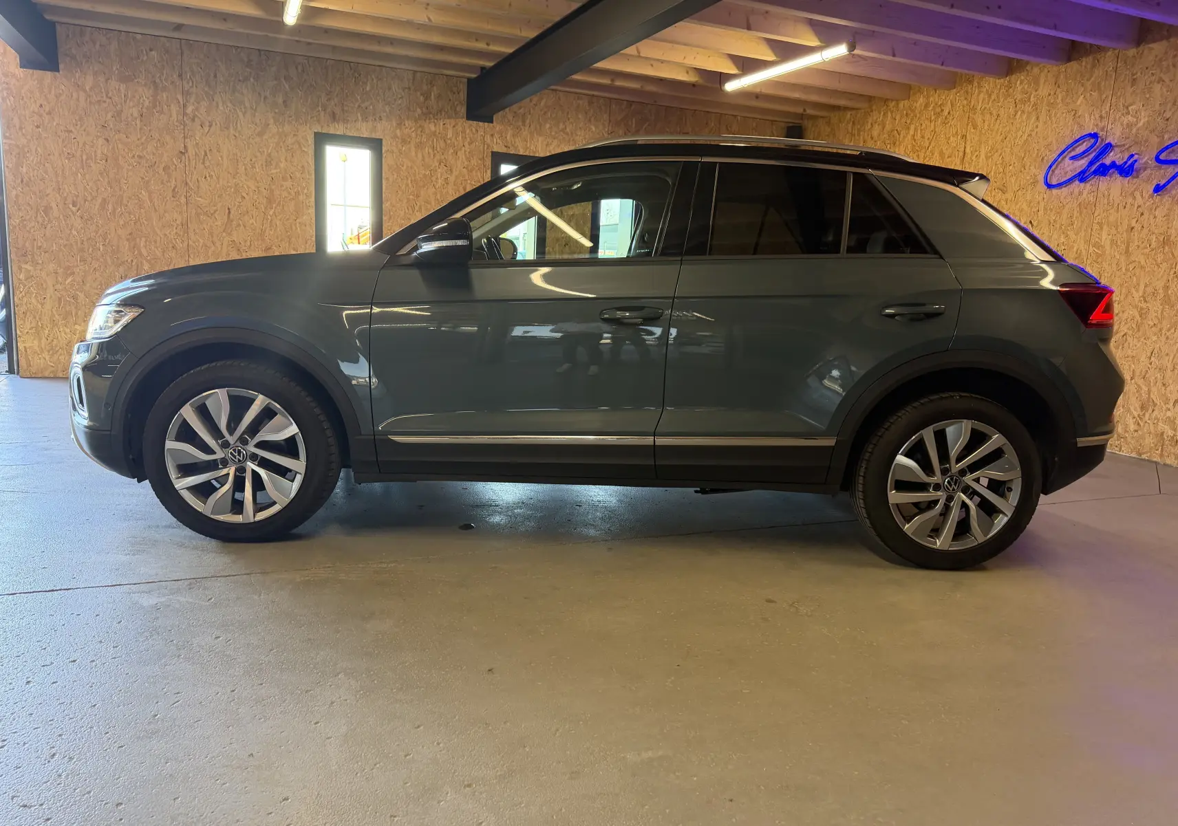 Vue de profil côté gauche d'un Volkswagen T-Roc bleu 2022, avec jantes alliage et toit noir en intérieur lumineux.