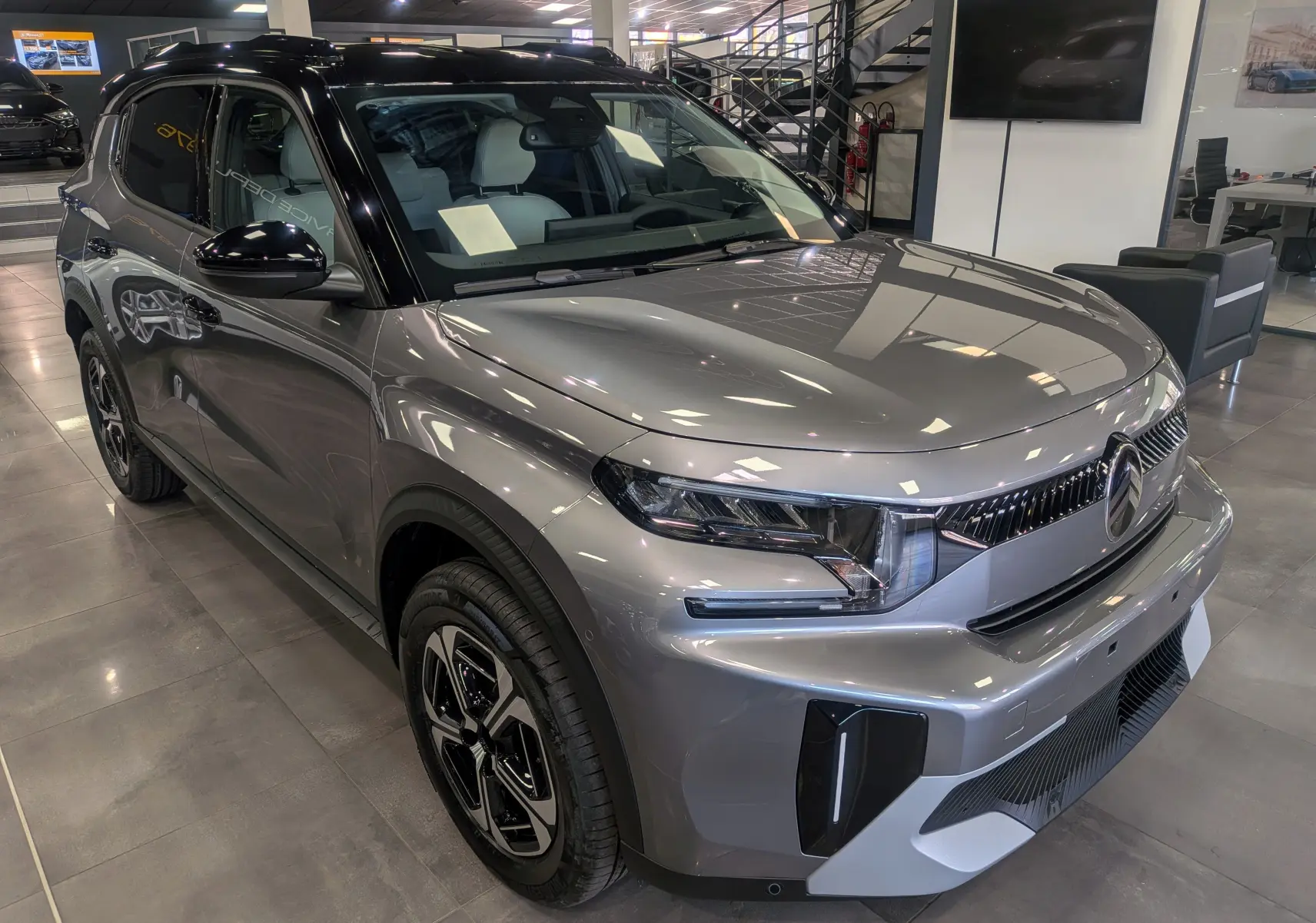 Vue 3/4 avant gauche du Citroën C3 Aircross hybride gris Mercury avec toit noir et jantes bi-ton en showroom.