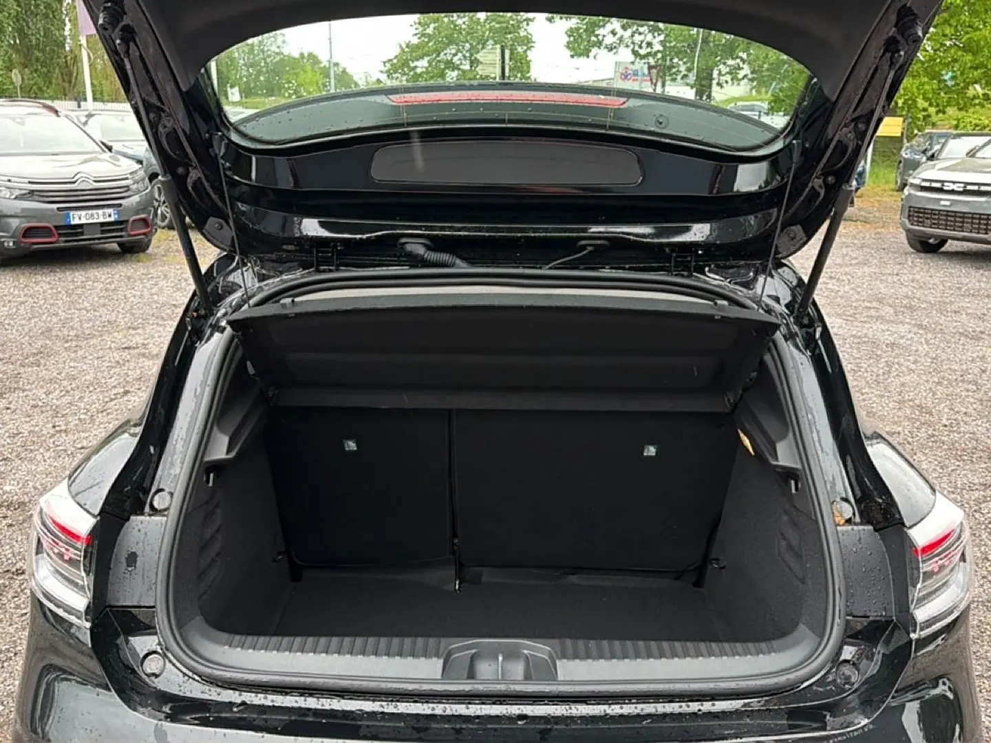 Coffre ouvert vu de l'arrière d'une Renault Clio V noire, montrant l'espace de chargement vide et les feux arrière LED.