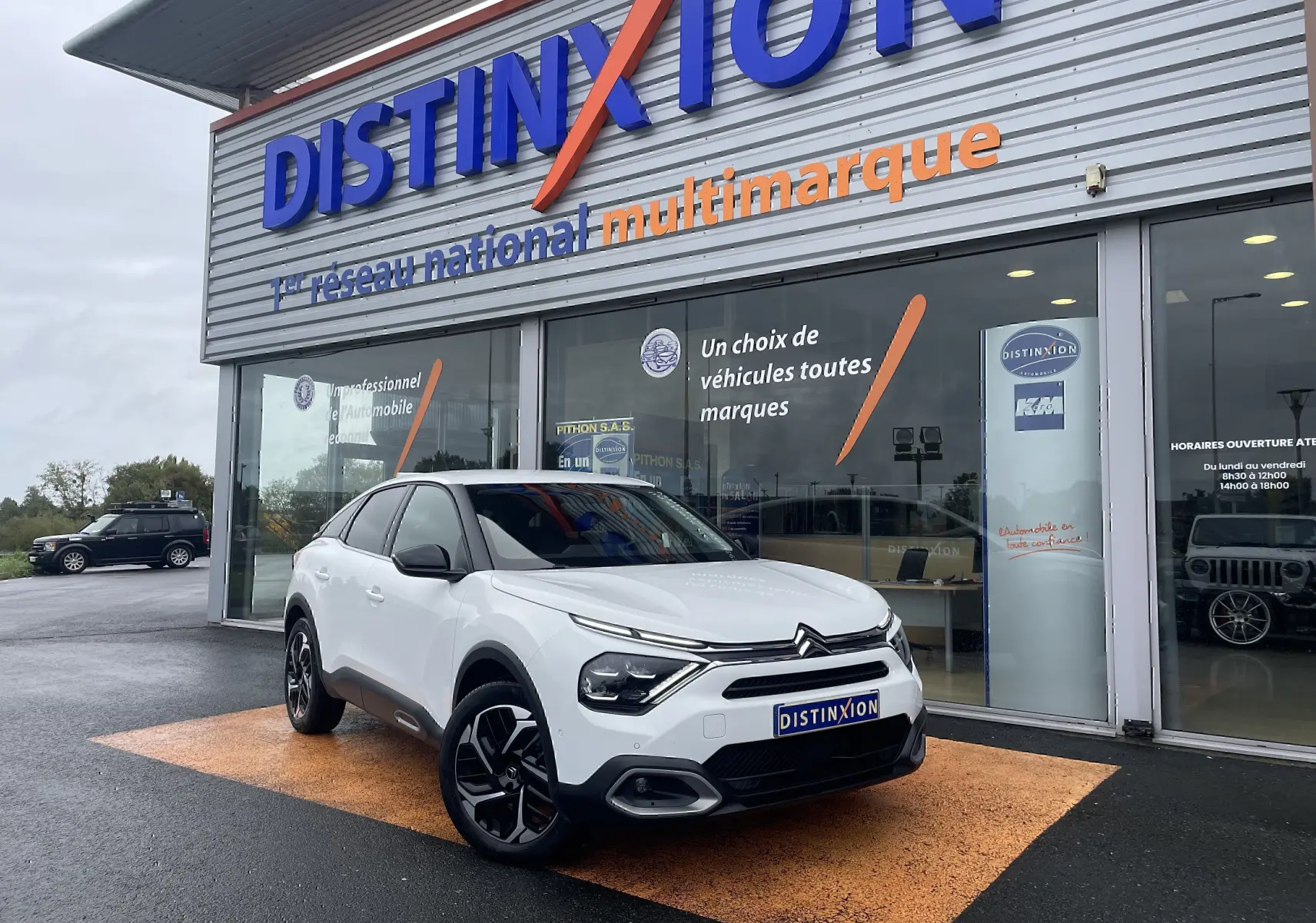 Citroën C4 blanc en 3/4 avant droit devant un showroom Distinxion, avec jantes noires et toit noir contrastant.