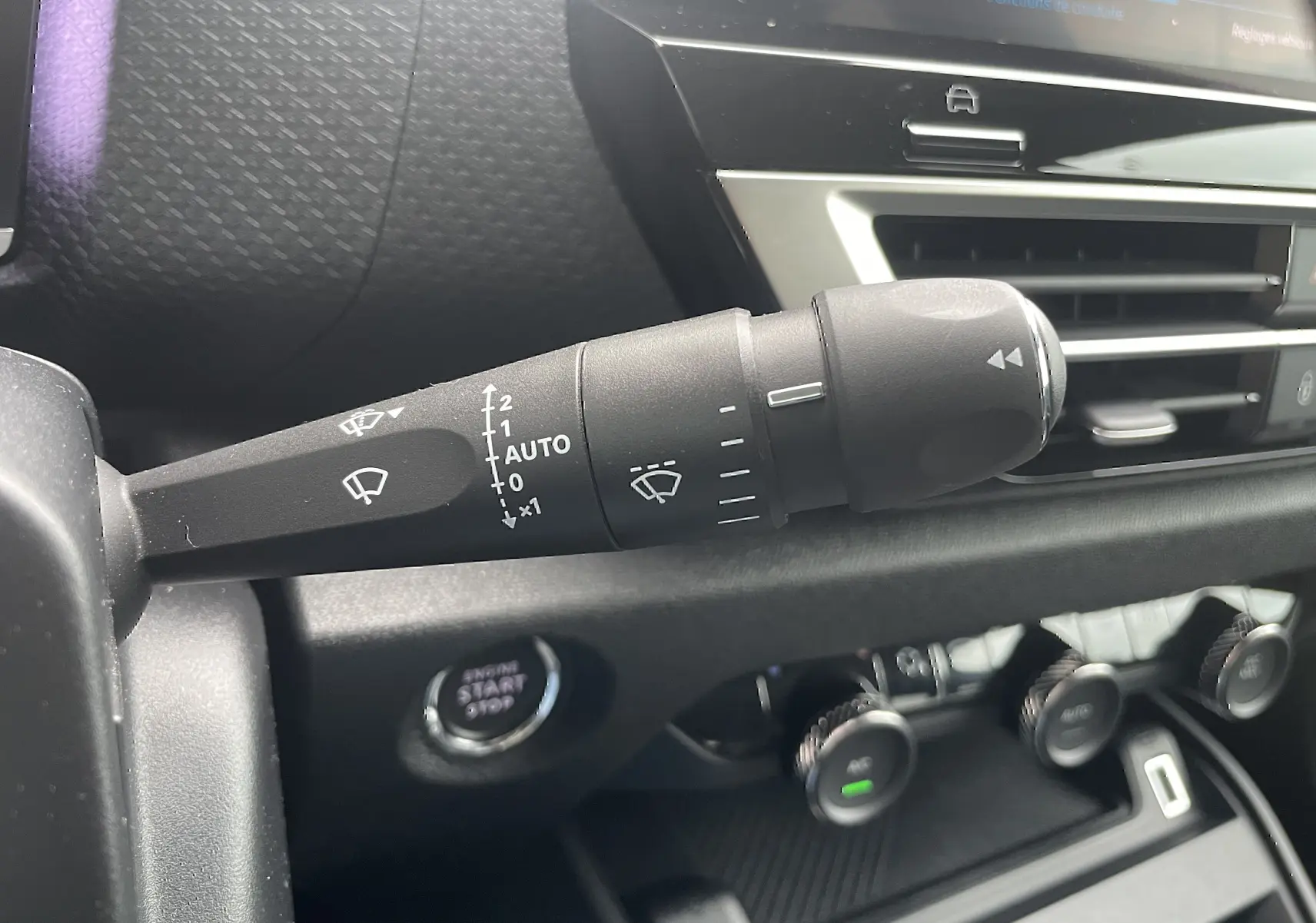 Gros plan sur la commande des essuie-glaces à gauche du volant dans l’habitacle gris-noir d’une Citroën C4 blanche 2022.