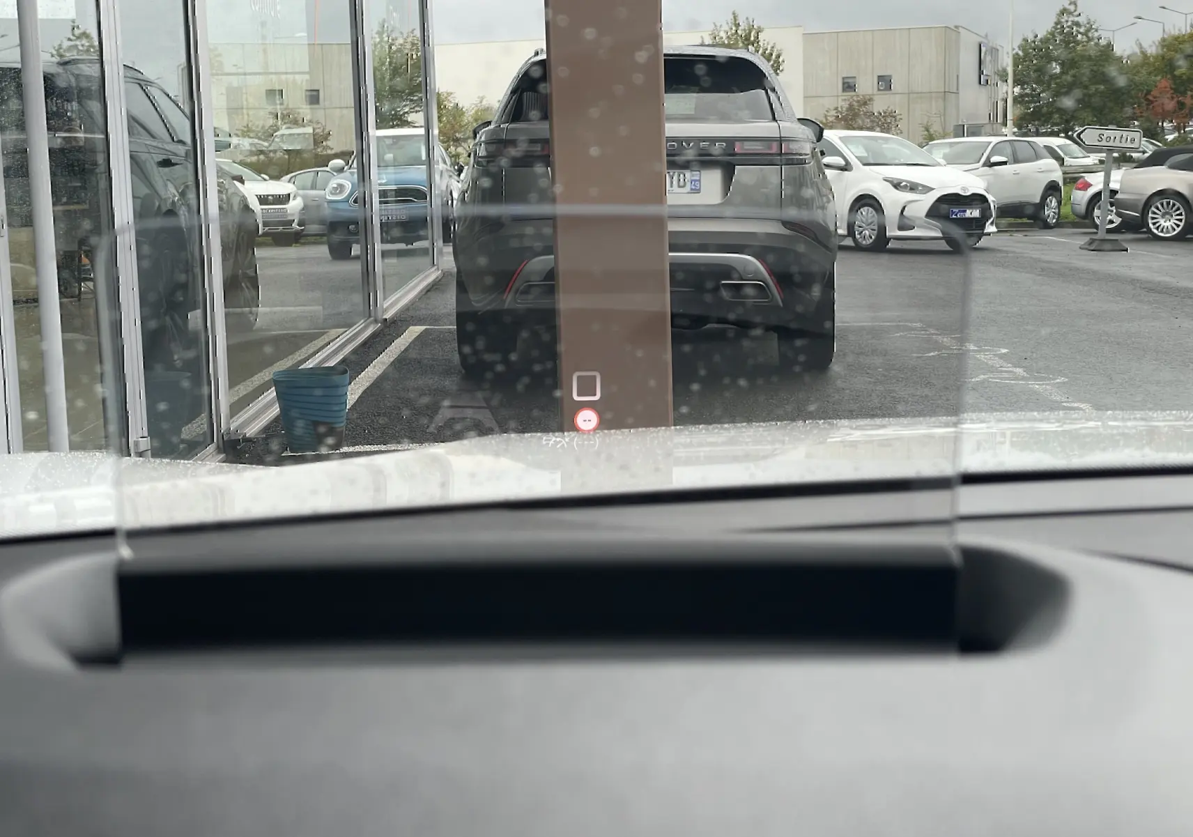 Vue depuis l'intérieur d'un véhicule blanc, montrant le pare-brise avec affichage tête haute et un SUV noir garé devant.