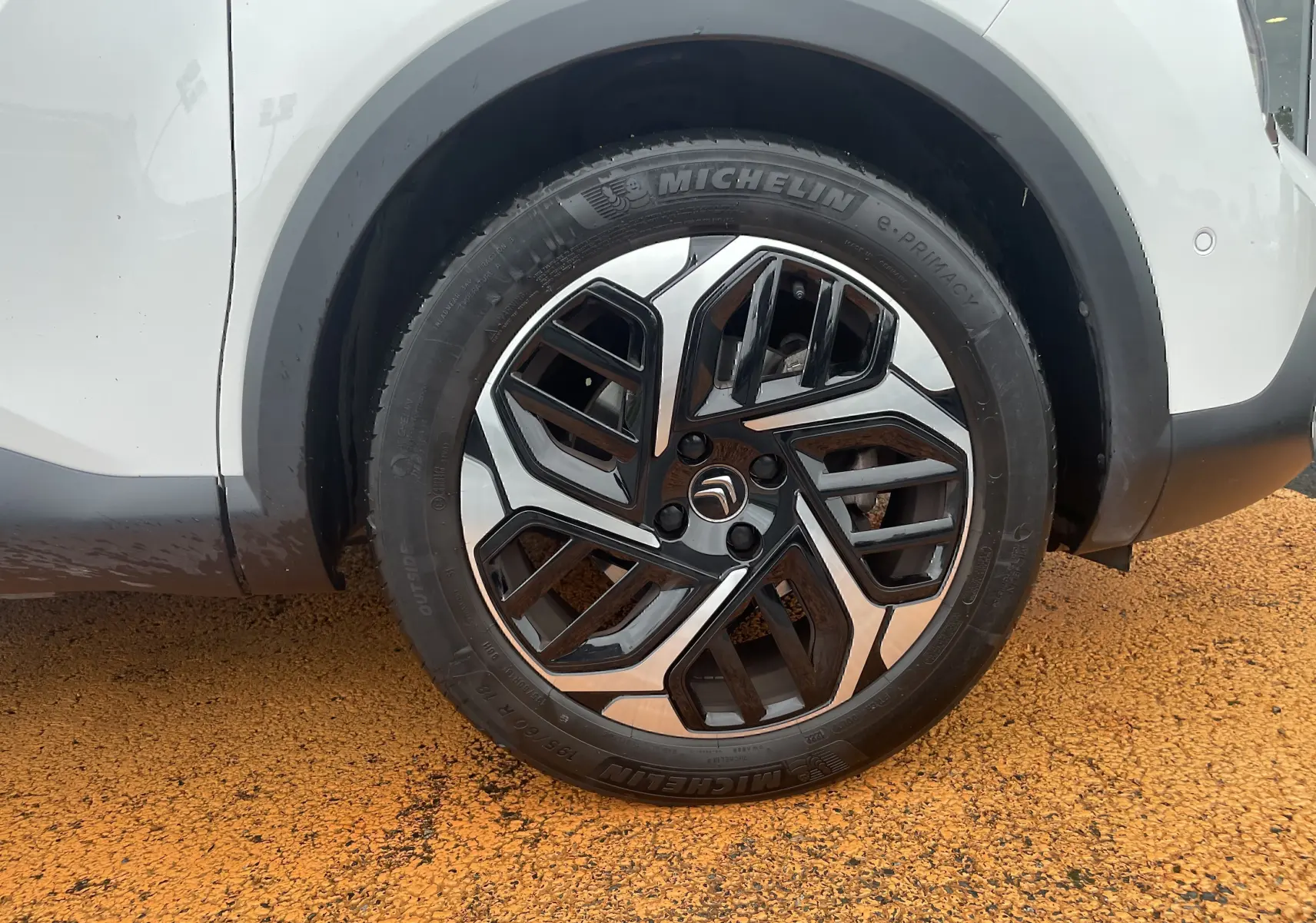 Gros plan sur la roue avant droite d'une Citroën C4 blanche, mettant en valeur la jante noire et argent au design moderne.