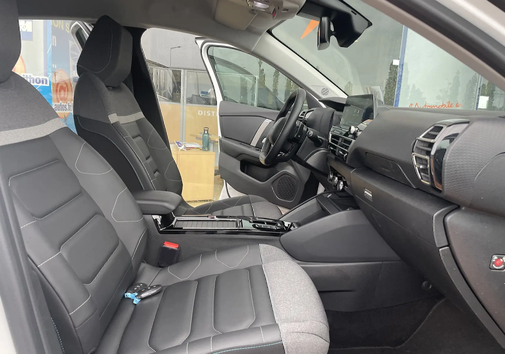 Vue intérieure côté conducteur de la Citroën C4 2022, sièges tissu gris noir avec console centrale brillante.
