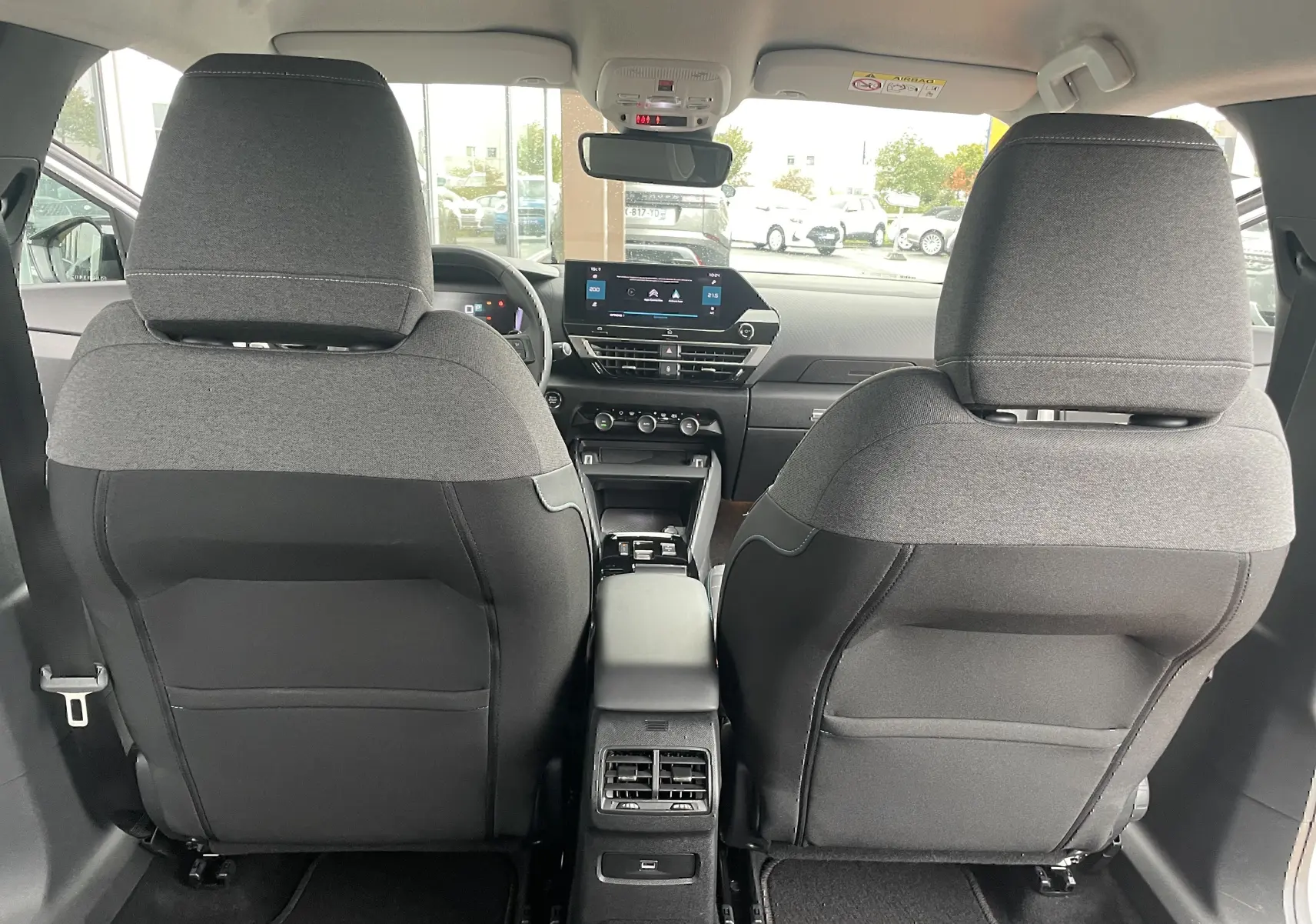 Vue intérieure arrière de la Citroën C4 2022 blanche, montrant les sièges tissu gris/noir et la console centrale avec écran tactile.