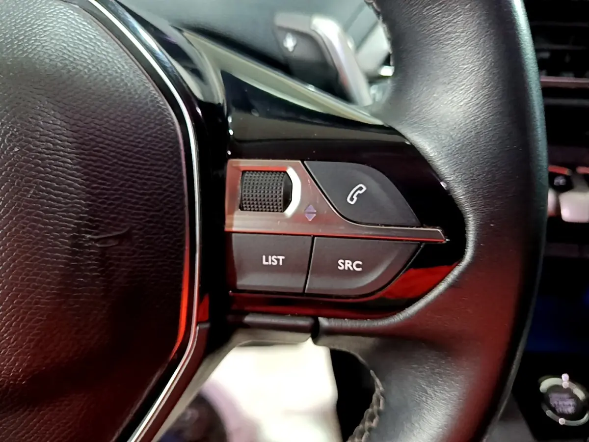 Gros plan sur le volant cuir noir de la Peugeot 3008 2022, avec commandes multifonctions et bouton appel téléphonique.