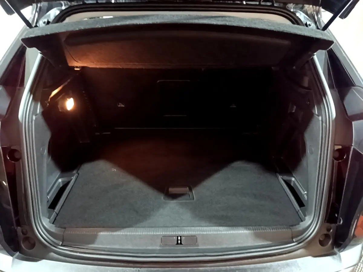 Coffre ouvert vu de l'arrière d'un Peugeot 3008 noir, montrant un espace de chargement propre et éclairé.