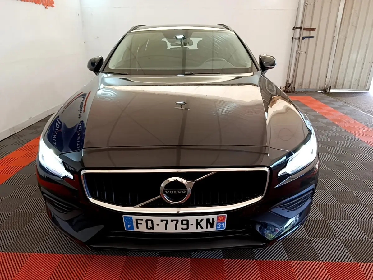 Vue avant d'une Volvo V60 noire 2020 avec phares LED allumés dans un garage au sol damier noir et rouge.