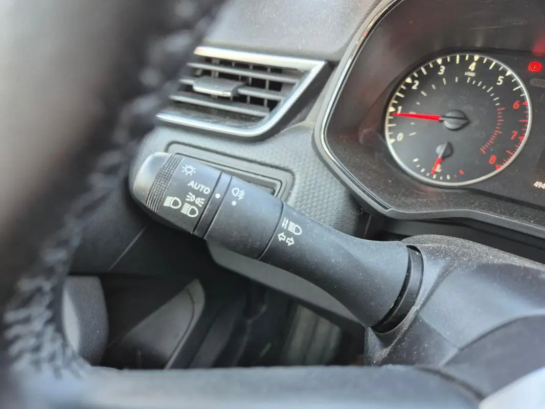 Gros plan sur la commande des phares et clignotants à gauche du volant dans une Renault Clio noire, tableau de bord visible.