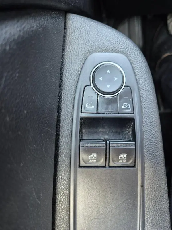 Gros plan sur les commandes de réglage des rétroviseurs et des vitres électriques côté conducteur d’une Renault Clio noire.