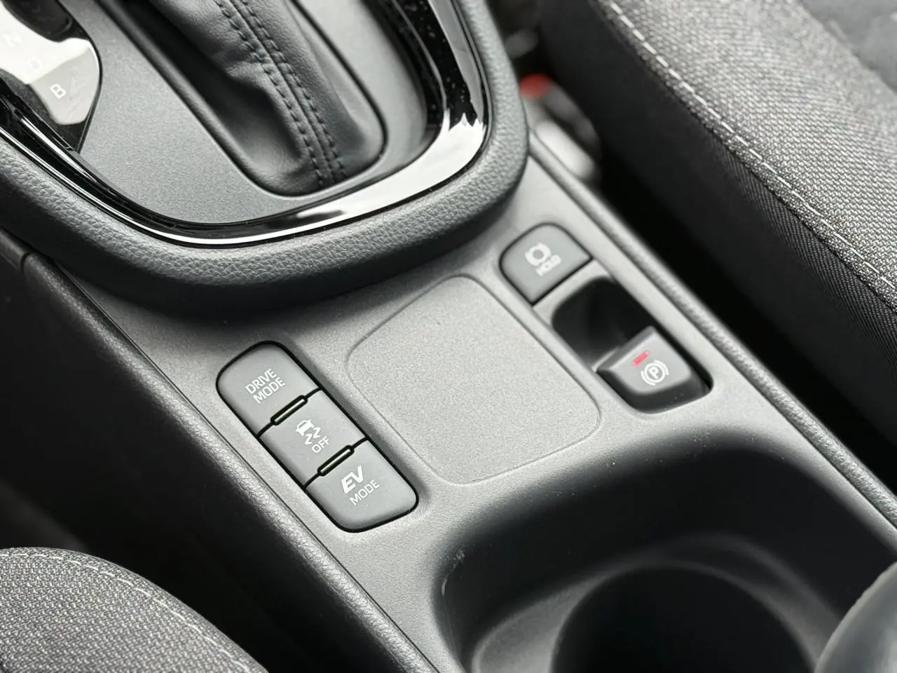 Gros plan sur la console centrale du Toyota Yaris Cross 1.5 Hybrid 116 Design avec commandes Drive Mode et frein à main électrique.