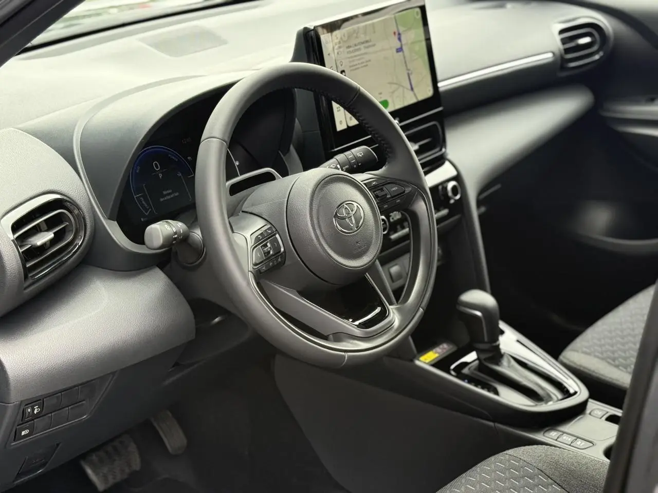 Vue intérieure côté conducteur de la Toyota Yaris Cross 2026, volant cuir, écran tactile vertical et levier de boîte auto.