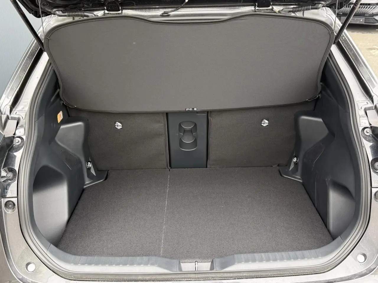 Coffre ouvert vu de l'arrière d'une Toyota Yaris Cross gris Atlas, montrant un plancher plat et un cache-bagages.