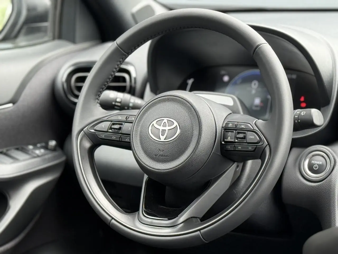 Vue rapprochée du volant cuir noir de la Toyota Yaris Cross 1.5 Hybrid 116 Design avec commandes intégrées.