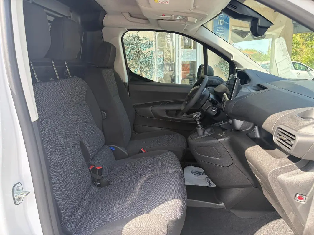 Vue intérieure côté conducteur du Peugeot Partner blanc 2026, montrant sièges tissu, volant multifonctions et tableau de bord avec GPS tactile.