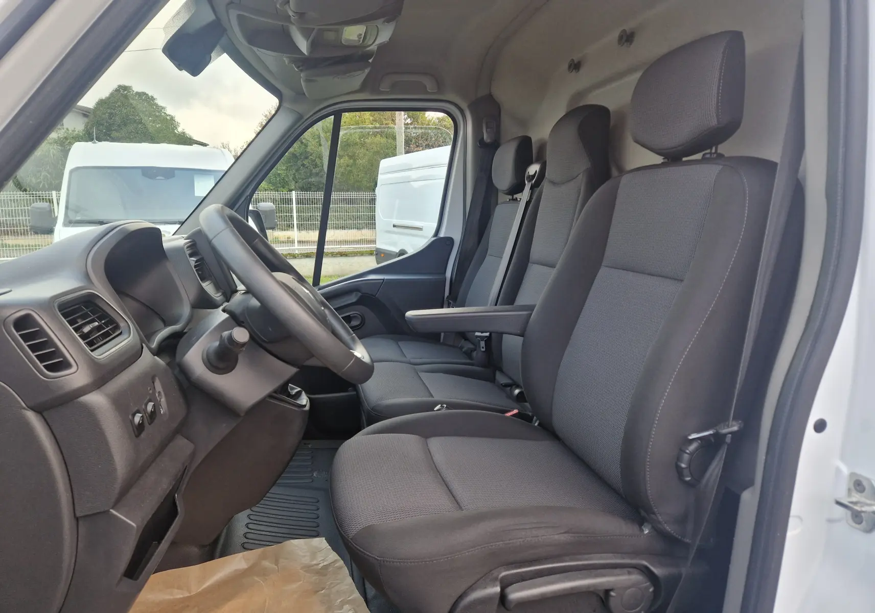 Vue intérieure côté conducteur du Renault Master blanc 2020, montrant les sièges noirs et le volant multifonction.