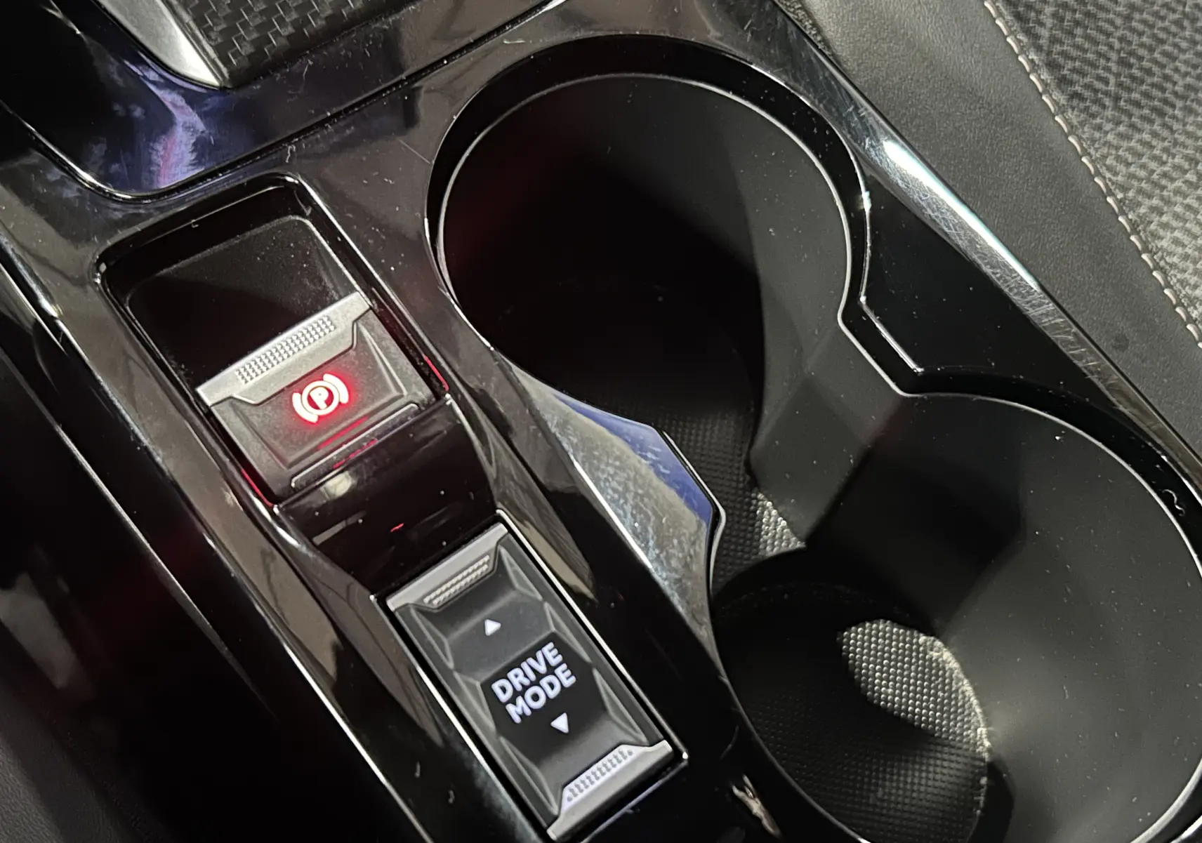 Gros plan sur la console centrale noire brillante du Peugeot 2008 Allure Hybrid 145, montrant le bouton Drive Mode et frein à main électronique.
