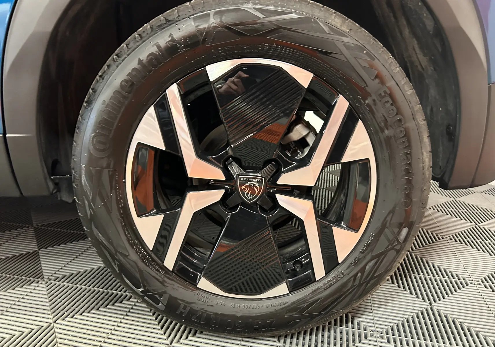 Gros plan sur la jante avant droite du Peugeot 2008 Allure Hybrid 145 bleu Obsession, avec design noir et argenté distinctif.