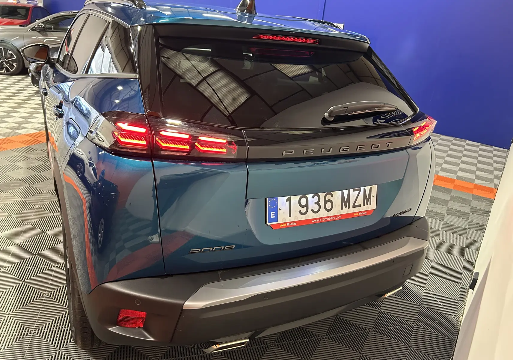 Vue 3/4 arrière d’un Peugeot 2008 Allure Hybrid 145 bleu Obsession avec feux arrière allumés et toit noir brillant.