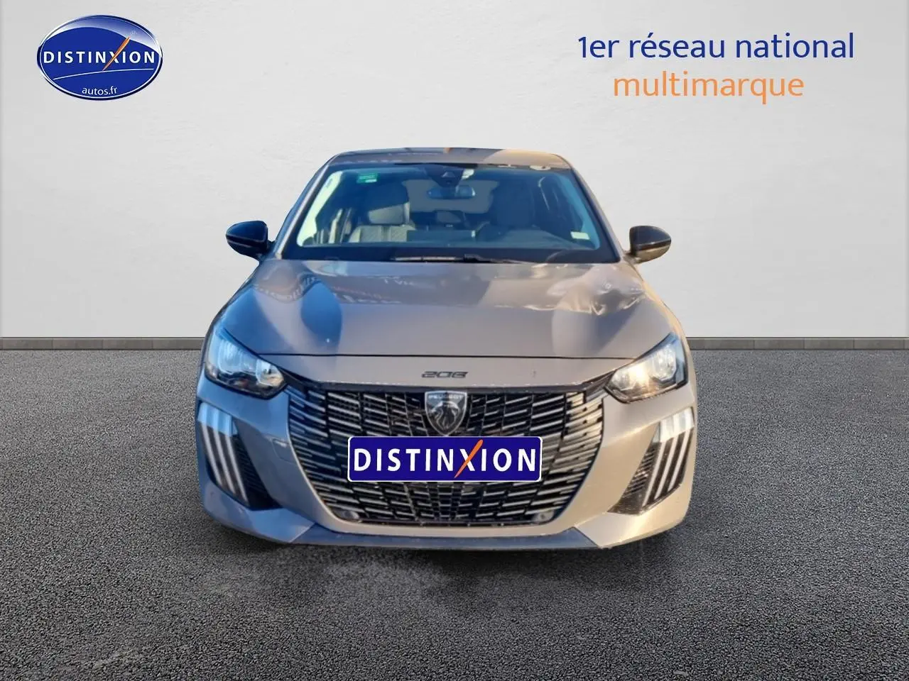 Vue frontale d'une Peugeot 208 1.2 PureTech 100 Allure gris Sélénite avec calandre noire distinctive et phares LED allumés.