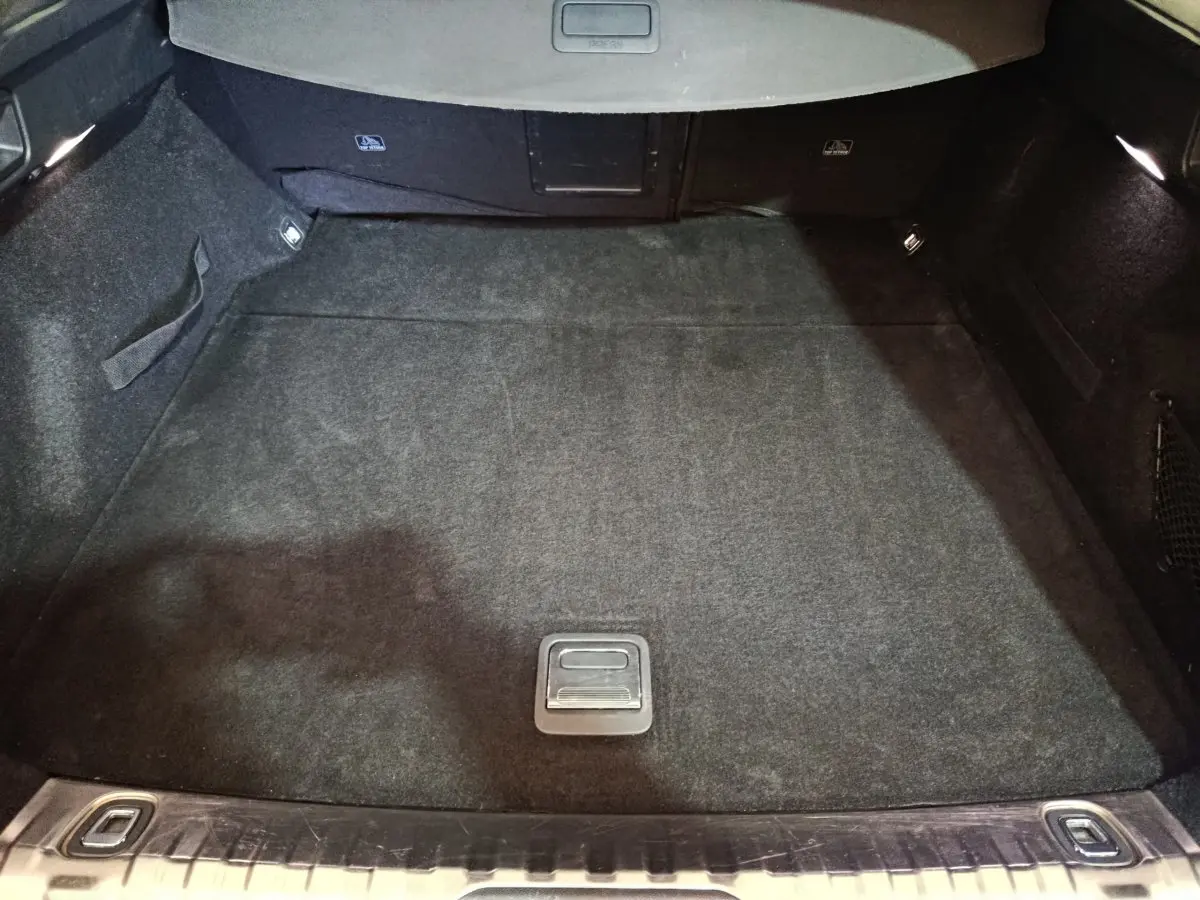 Coffre spacieux de Peugeot 508 gris clair vu de l'arrière, avec tapis noir et éclairage intérieur aux côtés.