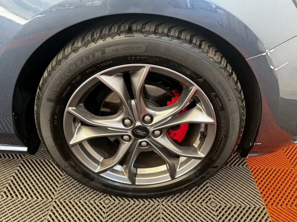Gros plan sur la roue avant droite d'une Ford Focus bleu, avec jante alliage et étrier de frein rouge visible.
