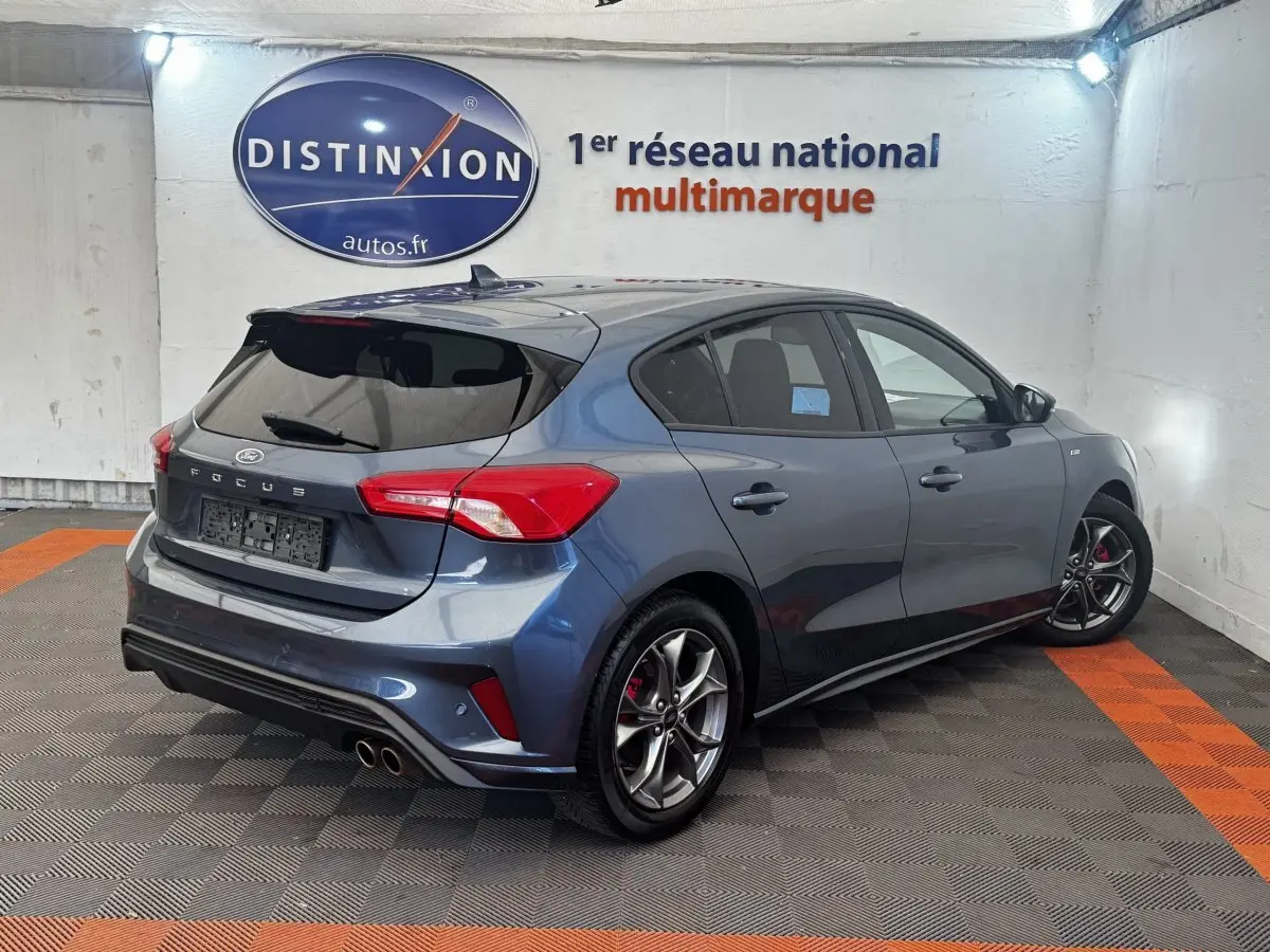 Vue 3/4 arrière droite d'une Ford Focus bleu métallisé avec jantes alliage et double sortie d'échappement sportive.